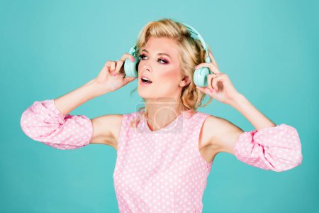 Foto de Chica DJ. Mujer rubia joven en auriculares escuchando música aislada en el fondo azul del estudio - Imagen libre de derechos