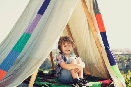 Téléchargez les photos : Enfant assis dans une tente au camp d'été. Enfant mignon passer des vacances d'été à la campagne. Le rêve du camp. Rêves d'enfants en tente extérieure. Rêve d'enfance. Enfant rêveur. Rêves et imagination. Enfants rêveurs - en image libre de droit