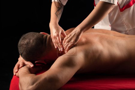 Foto de Hombre teniendo masaje en el salón de masajes. Masaje deportivo. Terapeuta masajeando hombros de un atleta masculino, trabajando con músculo trapecio. Hombre disfrutando de masaje en spa - Imagen libre de derechos