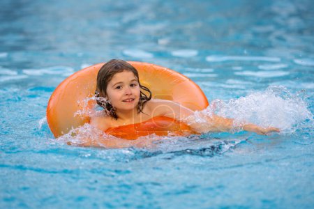 Téléchargez les photos : Heureux jeune enfant profitant de vacances d'été en plein air dans l'eau dans la piscine. Mignon petit enfant en maillot de bain nager sur un anneau gonflable. Enfant flottant dans une piscine - en image libre de droit
