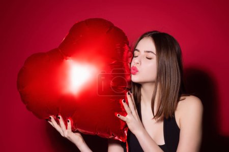 Foto de Hermosa joven sosteniendo globos rojos en forma de corazón, día de San Valentín. Cita romántica de mujer sexy. Mujer celebrando el Día de San Valentín. Retrato mujer bonita con forma de corazón globo rojo - Imagen libre de derechos
