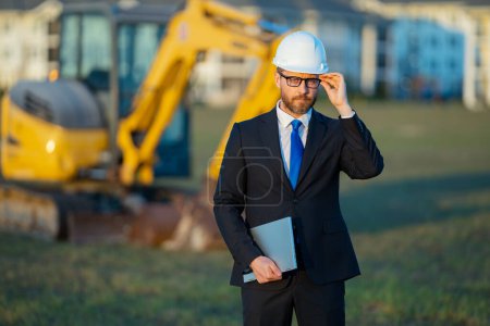 Photo for Construction builder investor. Man investor in front of construction site. Successful handsome man standing at modern home building construction. Portrait of midlle aged investor in suit and helmet - Royalty Free Image