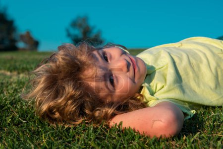 Foto de Retrato de un niño feliz tirado en el césped del parque. Sueño de verano. Sueños de niños en la hierba. Sueño de infancia. Un niño soñador. Sueños e imaginación. Cara de niños soñadores. Diversión de verano - Imagen libre de derechos