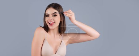 Téléchargez les photos : Beautiful woman applies brow gel with brows brush to her eyebrow. Studio portrait of young woman doing her eyebrow natural make up. Eyebrows make up concept - en image libre de droit
