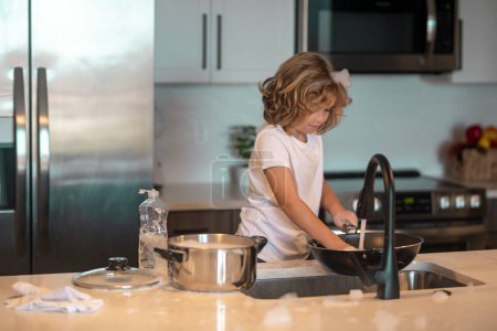 Téléchargez les photos : Lave-vaisselle pour enfants dans la cuisine intérieure. Enfant aidant ses parents avec les travaux ménagers. Petit garçon qui lave la vaisselle dans la cuisine intérieure. Enfant aidant ses parents avec les travaux ménagers - en image libre de droit