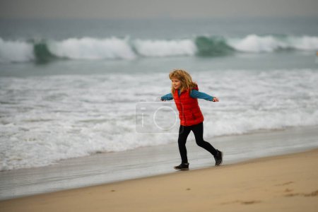 Téléchargez les photos : Enfant sportif courant dans la nature. Des enfants qui courent sur la plage. Vacances d'été. Joyeux gamin jouant sur la plage. Bonne enfance - en image libre de droit