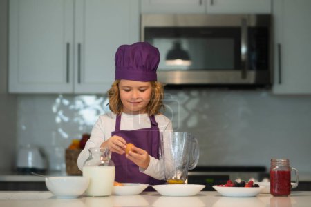 Téléchargez les photos : Cuisiner dans la cuisine. Petit garçon dans un chapeau de chef et un tablier de cuisine - en image libre de droit