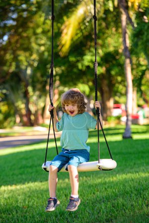 Foto de Little child having fun on a swing outdoor. Summer playground. Kid swinging high - Imagen libre de derechos
