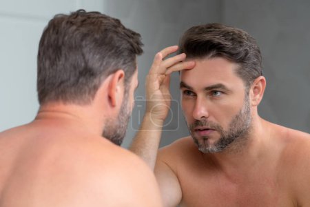 Close-up male wrinkles. Portrait of brunet man touching skin wrinkles. Middle aged man with touch wrinkles in front of the mirror. Aged skin. Man 40s cosmetic, skin treatment. Male face with wrinkles