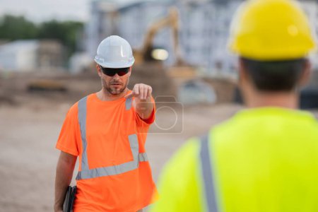 Photo for Construction worker with hardhat helmet on construction site. Construction engineer worker in builder uniform near construction building. Portrait of builder man in a site build house - Royalty Free Image