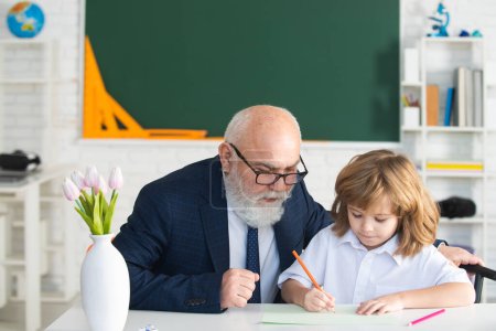 Photo for Happy kid in school. Old senior teacher help to writing. Education, teachering, elementary school. Private lesson - Royalty Free Image
