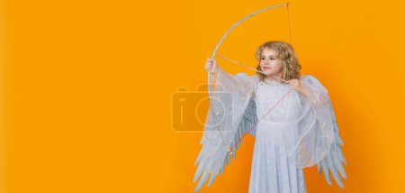 Photo for Kid angel with bow and arrow. Valentines day. Blonde cute child with angel wings on a yellow studio background. Wide banner panoramic header - Royalty Free Image
