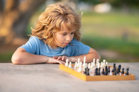 Foto de Niño jugando al ajedrez en el patio trasero, tendido en la hierba. Un niño concentrado juega ajedrez. Niño jugando juego de mesa al aire libre. Colegial ajedrecista pensador - Imagen libre de derechos