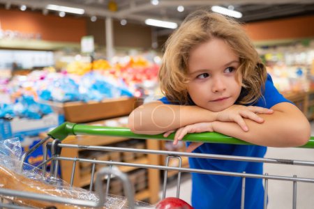 Téléchargez les photos : Enfant avec caddie à l'épicerie. Enfant au supermarché aux légumes. Petit enfant qui choisit de la nourriture en magasin ou à l'épicerie - en image libre de droit