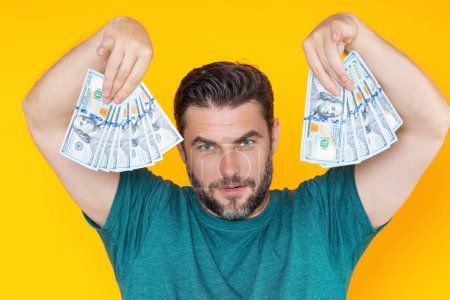Man holding cash money in dollar banknotes on isolated yellow background. Studio portrait of businessman with bunch of dollar banknotes. Dollar money concept. Career wealth business. Cash dollar