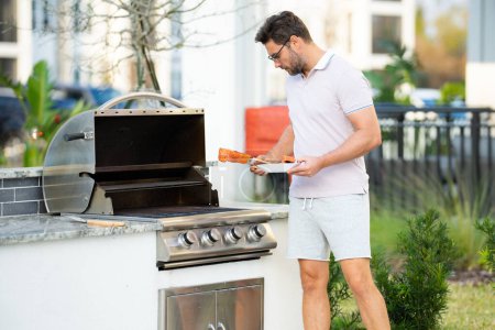 Photo for Male chef grilling and barbequing in garden. Barbecue outdoor garden party. Handsome man preparing barbecue salmon fillet. Concept of eating and cooking outdoor during summer time - Royalty Free Image