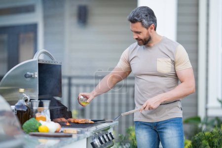 Photo for Barbecue concept. Middle aged hispanic man in t-shirt for barbecue. Roasting and grilling food. Roasting meat outdoors. Barbecue and grill. Cooking meat in backyard - Royalty Free Image