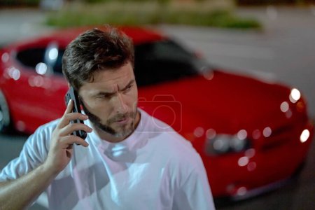 Photo for Aggressive brutal man talking on phone outdoor. Hipster guy talking on phone near car on night city street. Serious man talking on phone. Pensive handsome hipster look brutal, talking on phone - Royalty Free Image