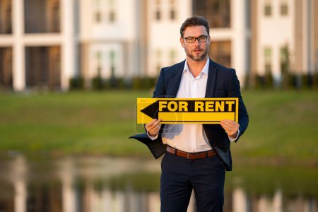 Photo for Handsome real estate agent holding banner house for rent. Real estate agent presenting the house for rent. Land agent trying to renting family house. Rent home, rental concept. Renting an apartment - Royalty Free Image