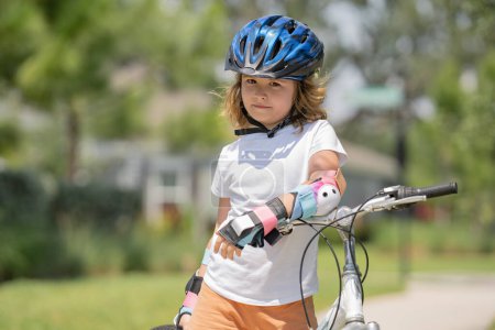 Photo for Boy in a helmet riding bike. Little cute adorable caucasian boy in safety helmet riding bike in city park. Child first bike. Kid outdoors summer activities. Kid on bicycle - Royalty Free Image