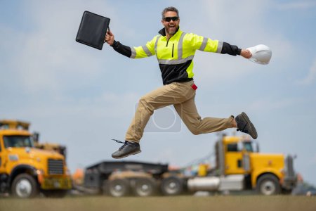 Photo for Construction man excited jump with helmet. Builder in helmet outdoor portrait. Worker in hardhat. Construction engineer worker in builder uniform on construction. Excited foreman jump - Royalty Free Image