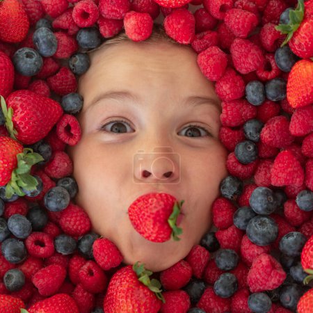 Foto de Comida saludable para niños. Cara infantil con bayas mezcla de fresa, arándano, frambuesa, mora - Imagen libre de derechos
