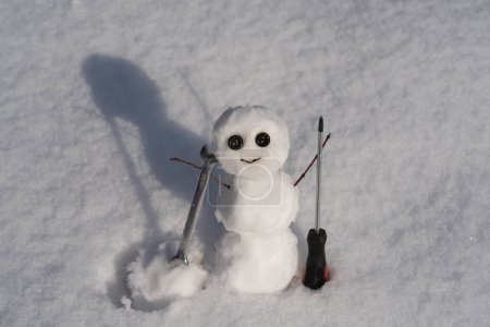 Téléchargez les photos : Bonhomme de neige. Bonhomme de neige drôle sur un terrain enneigé. Le matin avant Noël. Réparateur avec clé et tournevis. Soutien réparation et récupération de service - en image libre de droit