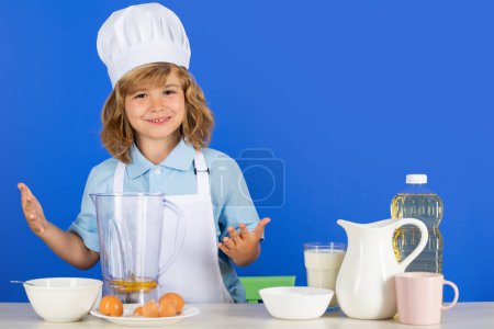 Foto de Niño chef aislado en azul. Chef divertido niño pequeño cocinero con gorra de cocinero uniforme y delantal cocinado comida en la cocina - Imagen libre de derechos