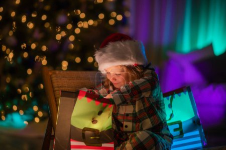 Foto de Niño con regalo presente con luz mágica. Iluminación regalo bolsa. Feliz Navidad y Feliz Año Nuevo. Niño celebrando la Nochebuena - Imagen libre de derechos