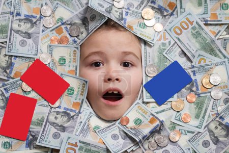 Téléchargez les photos : Enfant tête dans l'argent. Un gamin marrant avec de l'argent. Billets, pièces et cartes de crédit en dollars - en image libre de droit