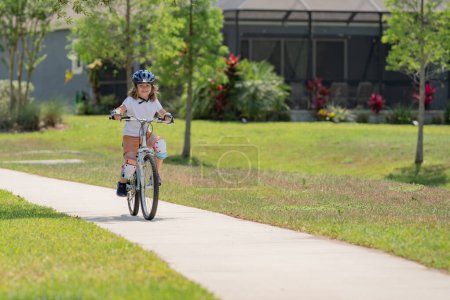 Foto de Lindo niño montando una bicicleta en el parque de verano. Los niños aprenden a conducir una bicicleta en un camino de entrada afuera. Niño montar en bicicleta en la ciudad con cascos como equipo de protección. Niño en bicicleta, bicicleta al aire libre - Imagen libre de derechos