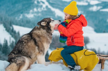 Téléchargez les photos : Traîneau de garçon, appréciant la promenade en traîneau. Enfant assis sur le traîneau avec chien husky sibérien. Les enfants jouent avec la neige. Concept vacances d'hiver - en image libre de droit