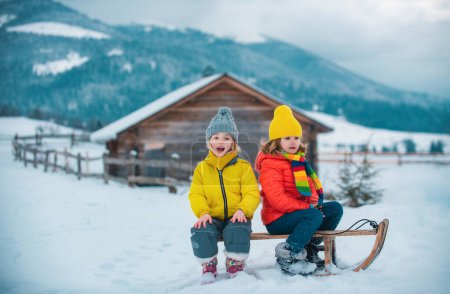 Téléchargez les photos : Enfant garçon et petite fille profitant d'une balade en traîneau. Enfants faisant de la luge ensemble, jouant dehors dans la neige sur les montagnes en hiver - en image libre de droit