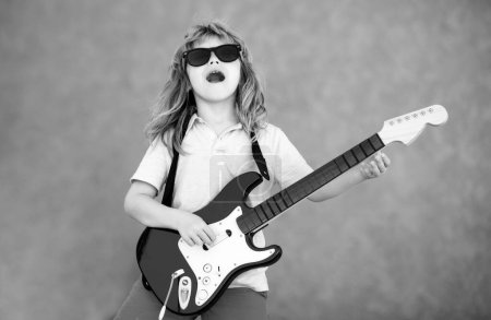 Téléchargez les photos : Rock and roll, petite rock star. Petit garçon jouant de la guitare en plein air. Musique pour enfants - en image libre de droit