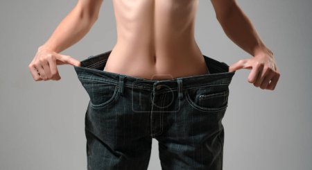 Téléchargez les photos : Une perte de poids réussie est une femme avec un jean trop grand après un régime. Pantalon surdimensionné dans le concept de perte de poids - en image libre de droit