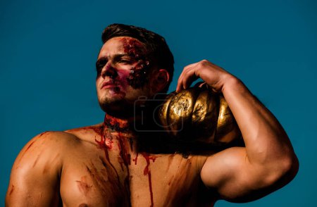 Photo for Young handsome man with muscular body posing in street holding halloween pumpkin. Halloween face art. Half face portrait. Halloween or horror concept - screaming walking dead zombie - Royalty Free Image