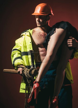 Photo for Hot sexy Firefighter. Firefighter sexy body muscle man holding saved sexy woman. Rescuer, firefighter, miners - risky occupations concept. Working profession, special clothes, overalls. - Royalty Free Image
