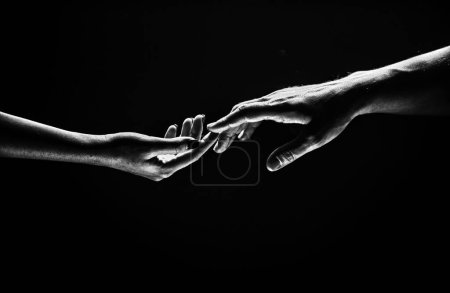 Romantische Berührung mit den Fingern, Liebe. Zwei Hände strecken einander, schwarzer Hintergrund. Verliebtes Paar, das hads hält, aus nächster Nähe. Helfende Hand, Unterstützung, Freundschaft. Zärtlichkeit, zarte Berührung