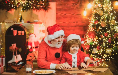 Photo for Christmas helper and Santa writing or reading letter home near the Christmas tree. Portrait of cheerful dreamy granny Santa and grandchild writing letter to Santa Claus - Royalty Free Image