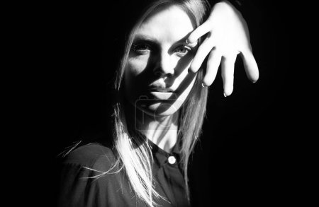 Photo for Shadow of hands on girls face, charming attractive female model. Serious woman with light on a black background. Beautiful female face in the darkness. Tender and seductive look. Fashion portrait - Royalty Free Image
