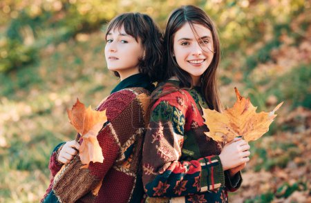 Téléchargez les photos : Les filles passent joyeusement du temps dans le parc d'automne. Deux filles avec des bouquets de feuilles d'automne. Deux filles blaguant avec des feuilles jaunes. Deux belles femmes dans le parc d'automne - en image libre de droit