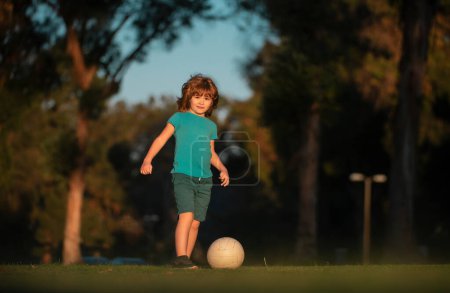 Foto de Niño jugando al fútbol en el campo con pelota de fútbol. Concepto de deporte infantil. Niño jugando al fútbol en el parque infantil - Imagen libre de derechos
