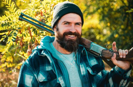 Foto de Fotos para Barbería. Hombre cazador barbudo sosteniendo arma y sonriendo. Cazador con barba larga a la caza. Barbería vintage. Ideas sobre Peluquería y Peluquería - Imagen libre de derechos