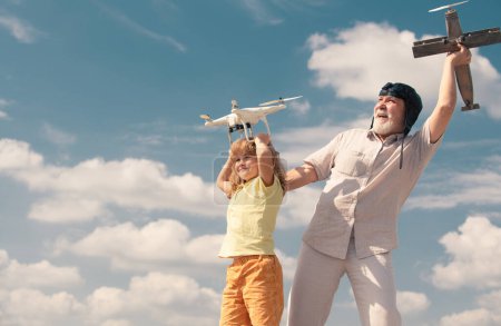 Téléchargez les photos : Grand-père et fils tiennent l'avion et le drone quadricycle contre le ciel. Enfant pilote aviateur rêvant de voler - en image libre de droit