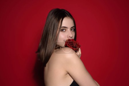 Foto de Retrato de estudio de belleza. Hermosa modelo con flor de rosa roja, aislada sobre fondo rojo estudio. Encantadora joven con maquillaje perfecto - Imagen libre de derechos
