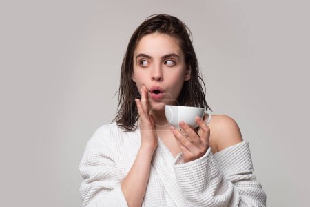 Foto de Divertido modelo sorprendido sosteniendo taza de café. Feliz mujer sonriente en albornoz con taza de café, estudio gris aislado - Imagen libre de derechos
