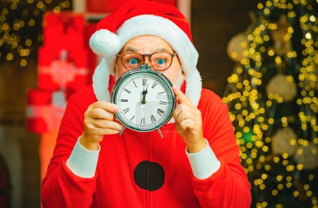 Téléchargez les photos : Père Noël - barbu drôle senior. Photo du Père Noël pointant vers l'horloge montrant cinq minutes à minuit. Noël. Nouvel an et Noël - en image libre de droit