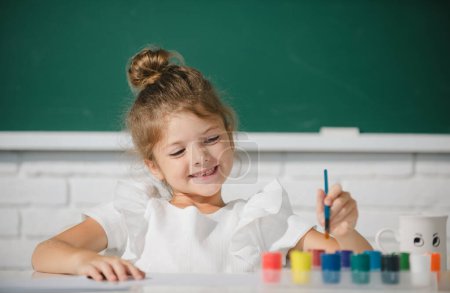Foto de Lección de escuela de pintura, dibujo artístico. Lindo niño preescolar niña dibujo en la escuela. Niña pintura en la escuela primaria - Imagen libre de derechos