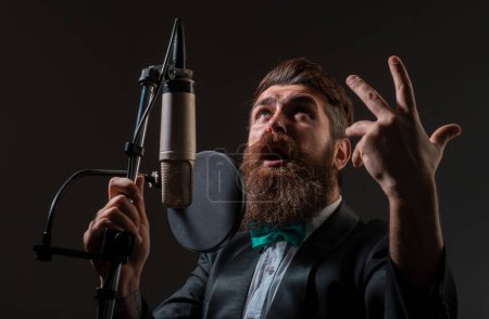 Téléchargez les photos : Un chanteur dans un studio d'enregistrement. Homme barbu expressif avec microphone. Chanteuse classique en costume - en image libre de droit