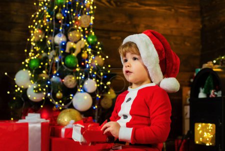 Téléchargez les photos : Les enfants de Noël. Enfant de Noël tenant une boîte cadeau rouge. Enfants de Noël - concept de bonheur. Joyeux enfant mignon ouvrant un cadeau de Noël - en image libre de droit